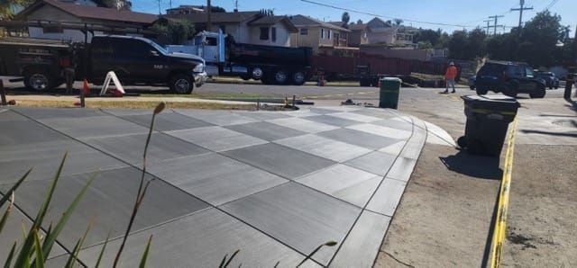 Checkerboard concrete sidewalk with nearby trucks and trash cans on a sunny day.