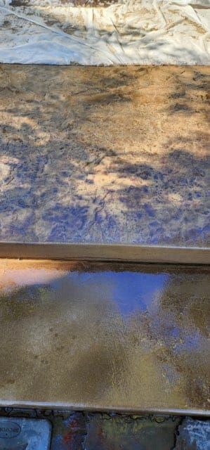 Close-up of a multi-toned, wet concrete surface reflecting a tree's shadow and light.