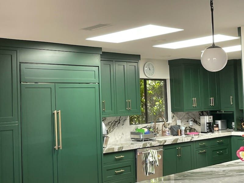Green kitchen cabinets, refrigerator, and counters; skylights; pendant light; stainless steel appliances.