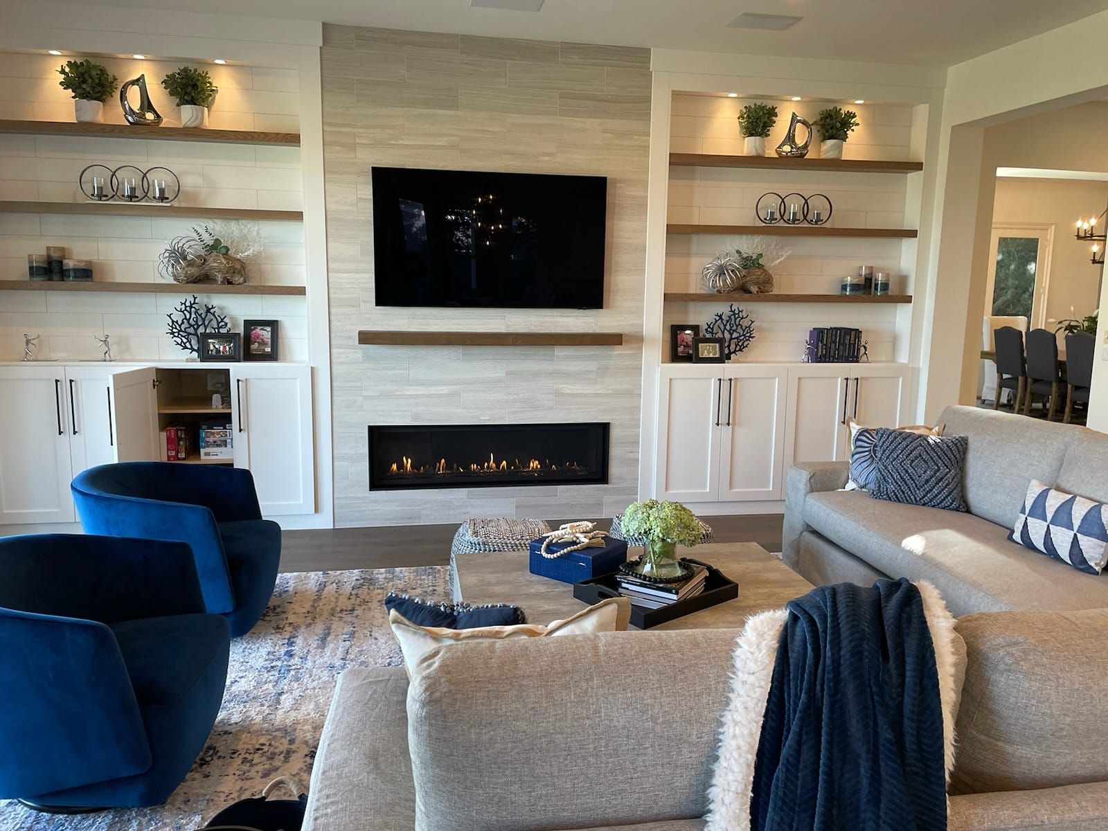 Living room with fireplace, built-in shelves, TV, two blue chairs, and a gray couch.
