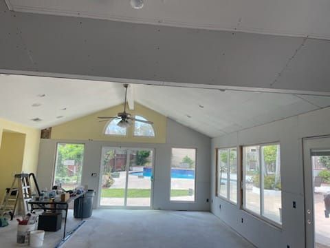 Interior of a room under construction with a vaulted ceiling, windows, and a view of a pool.