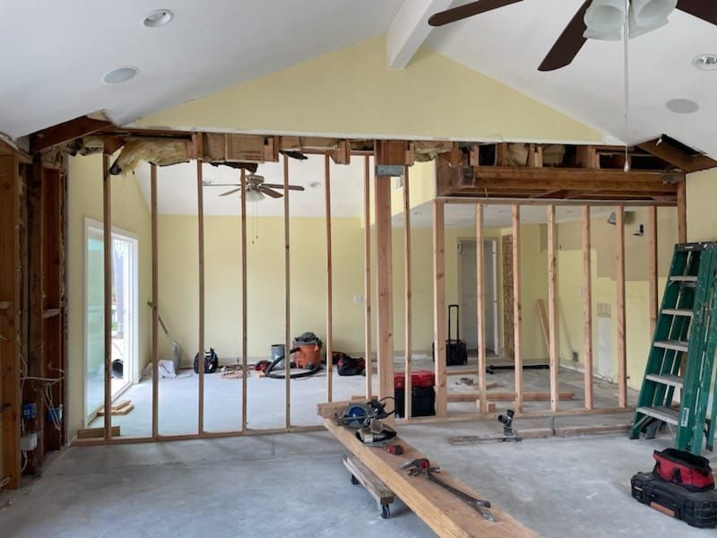 Interior framing of a room under construction with exposed beams, drywall removed, tools, and a ladder.
