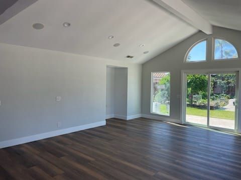 Empty living room with wood floor, high vaulted ceiling, and large windows overlooking a yard.