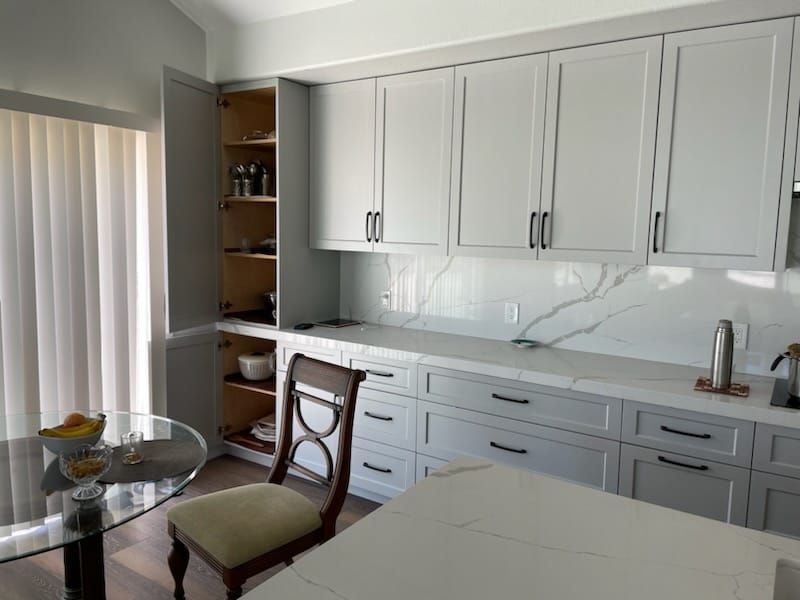Kitchen with gray cabinets, white countertops, a round glass table, and a wooden chair.