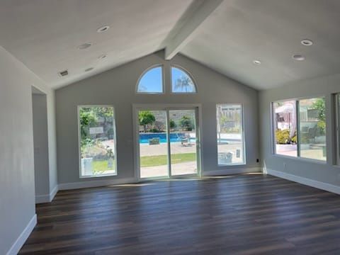 Empty room with dark wood floors and large windows overlooking a pool.