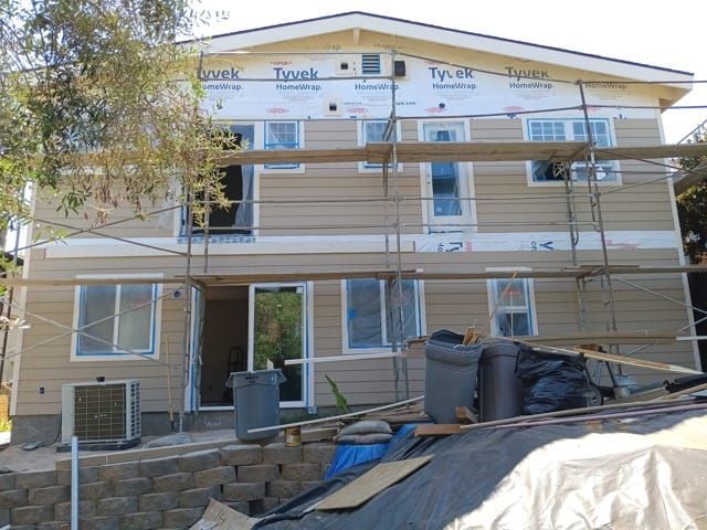 Two-story house under construction with tan siding, scaffolding, and windows.