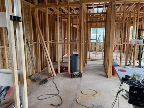 Interior view of a building under construction, wooden frames visible. Tools and construction materials are scattered about.