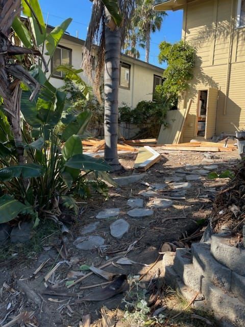 Backyard path with stepping stones, plants, and yellow house in background.