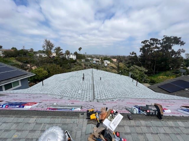 Roof in progress with tools, materials, and a distant neighborhood under a cloudy sky.