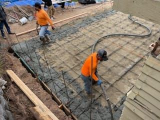 Workers pouring concrete onto a rebar grid in an outdoor construction site.