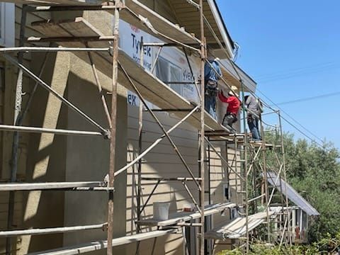 Construction workers on scaffolding installing siding on a house exterior.