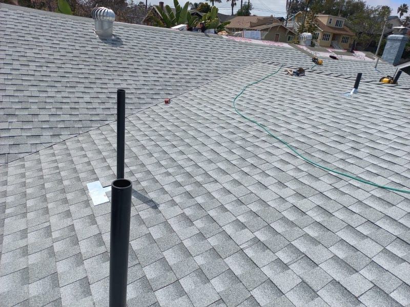 New asphalt shingle roof, gray with variations. Black pipe and vents visible. Rooftop setting.