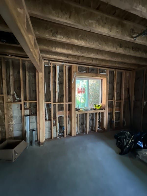 Basement interior, unfinished, with window. Wooden studs frame the walls. Concrete floor.