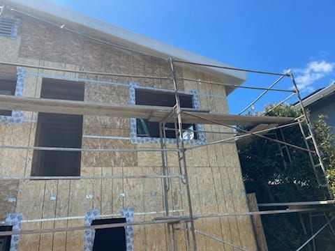 Building under construction; wood siding, windows, scaffolding, blue sky.
