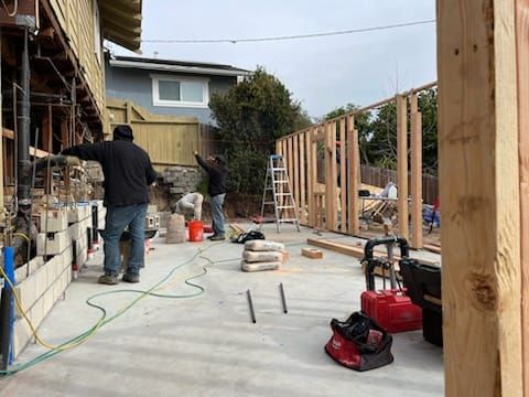 Construction workers building a structure outdoors. Wooden frame and concrete slab visible.