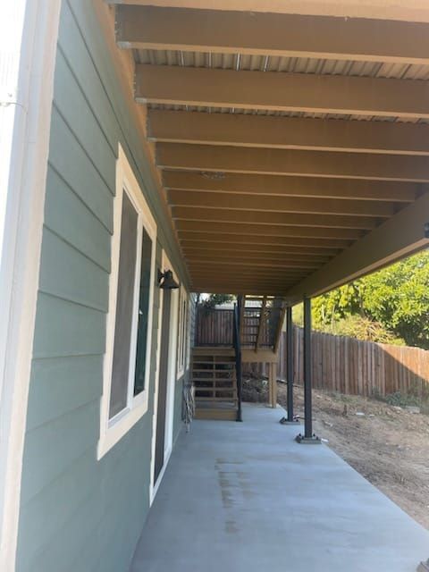 Exterior view of a house with blue siding, a covered porch, and a concrete patio. Stairs lead to the yard.