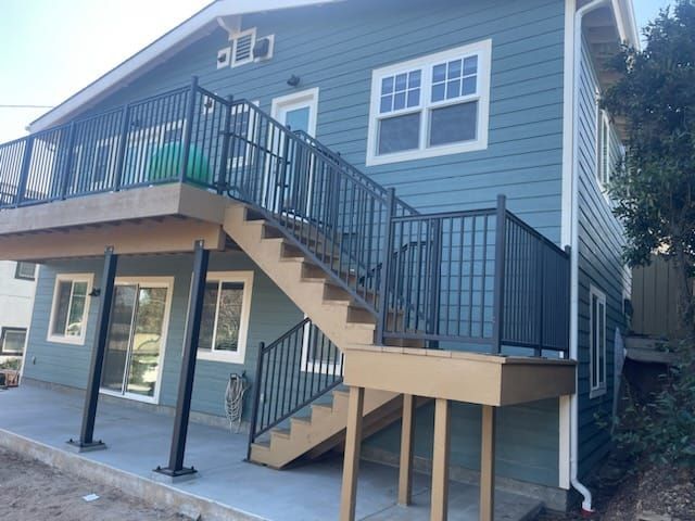 Two-story house with blue siding, a deck, stairs with black railings, and support posts.