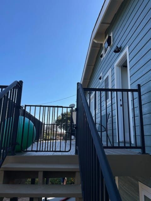Black metal railing on steps leading to a blue house with white door and clear sky.