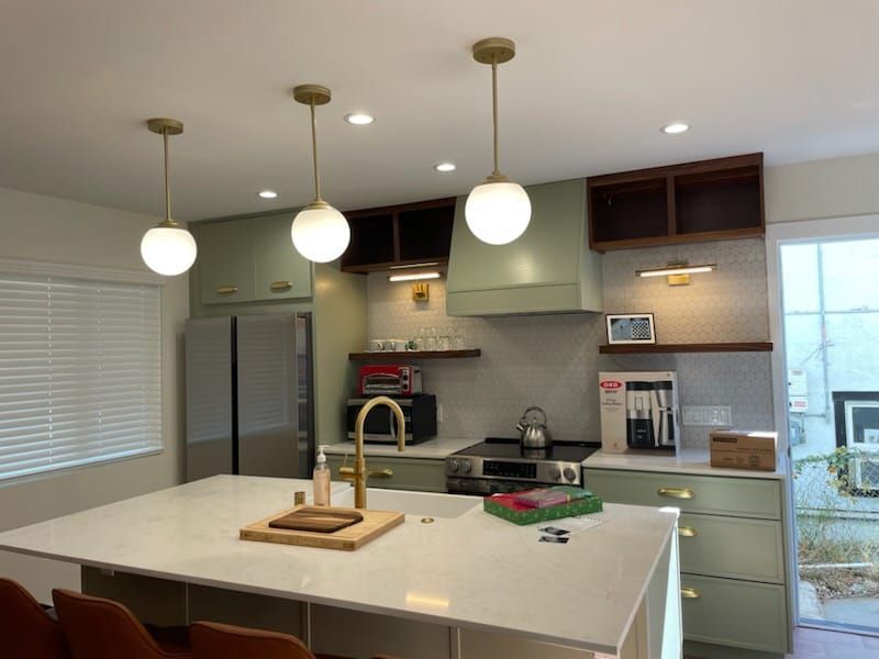 Kitchen with green cabinets, white island, gold fixtures, and globe pendant lights.