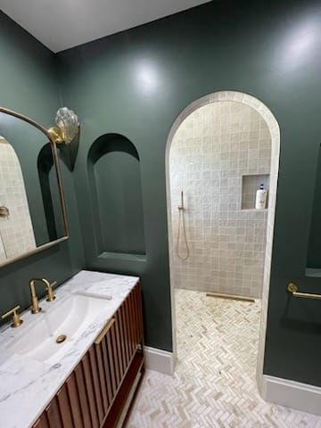 Green bathroom with archway to shower, marble counter, gold fixtures, and patterned floor.