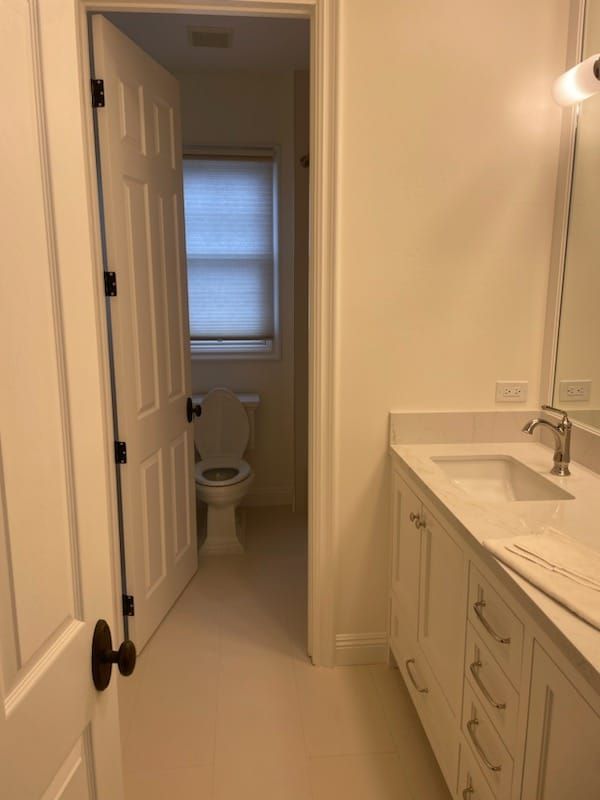 Bathroom with white walls, vanity, and a doorway leading to a toilet.