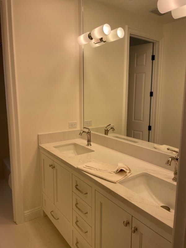 White bathroom with a double vanity, mirror, and overhead lights.