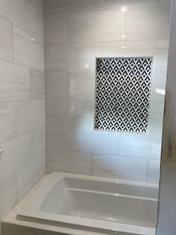 White tiled bathroom with built-in tub and decorative tile niche.