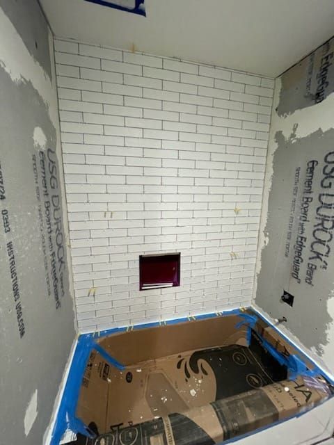 Bathroom wall partially tiled with white subway tile. A rectangular niche is present, and a blue tub is taped off.