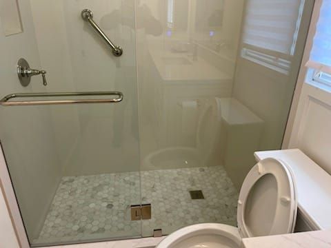 Bathroom with glass shower, grab bar, pebble tile floor, and toilet.