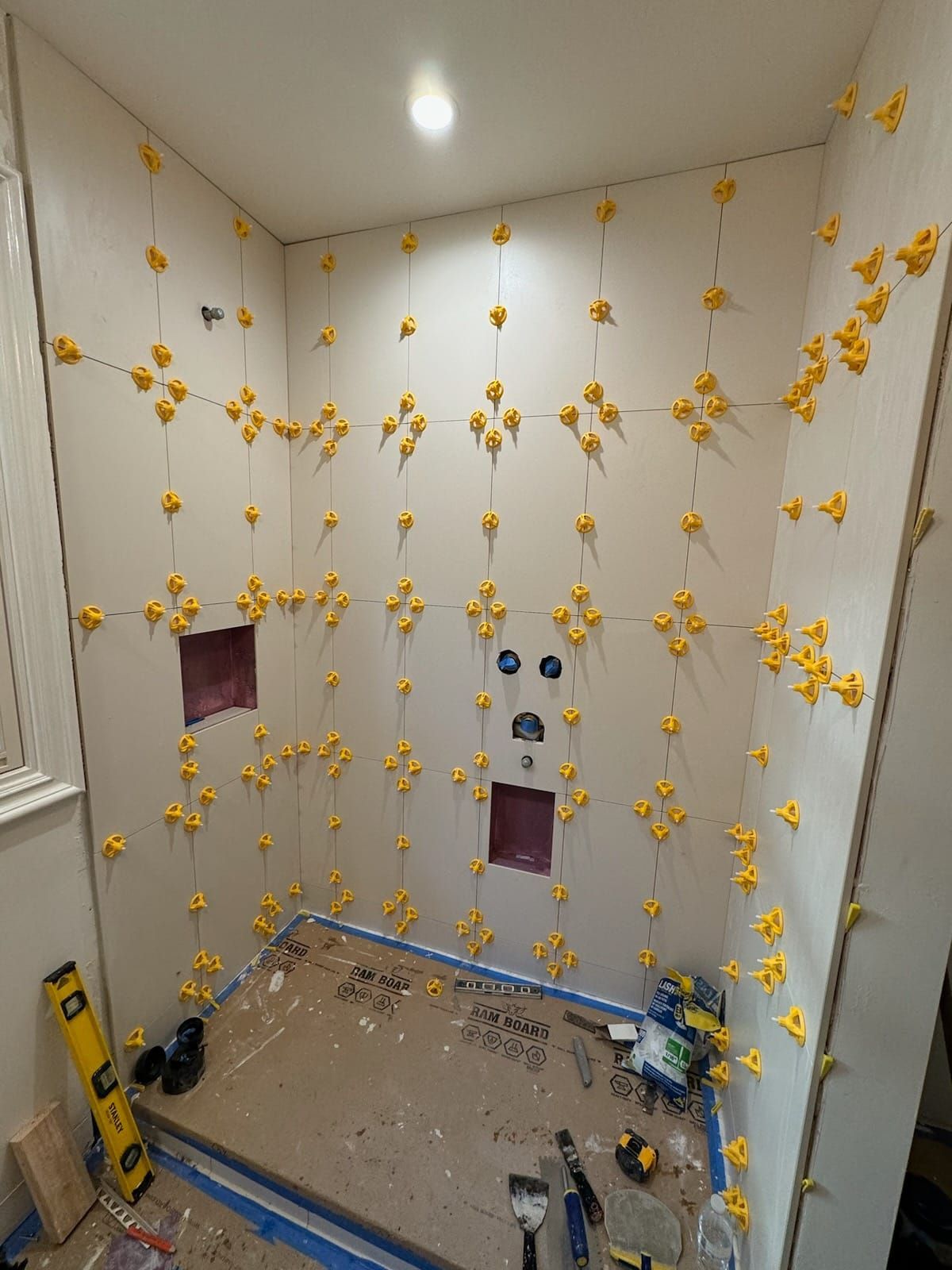 Bathroom walls with many yellow tile leveling clips. Tiles are partially installed around plumbing fixtures.