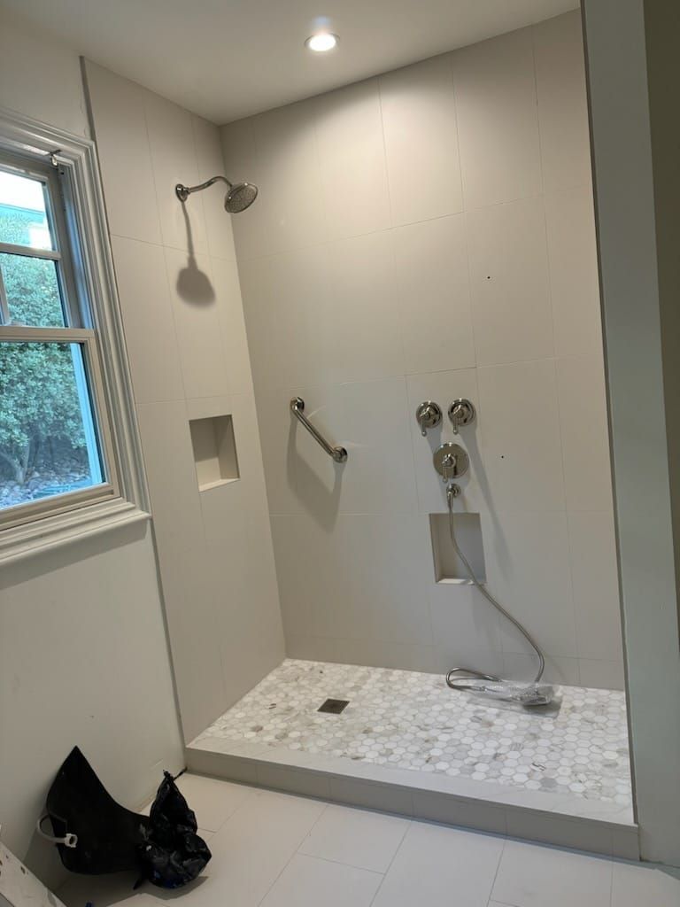 Neutral-toned handicap-accessible shower with grab bar, built-in soap niche, and pebbled floor.