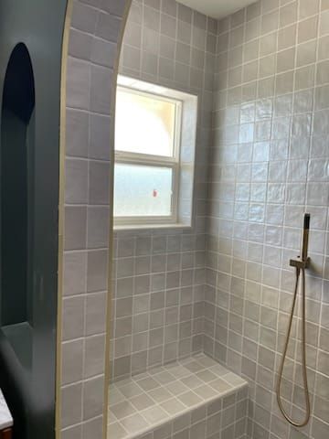 Gray tiled shower with a built-in bench and arched doorway.