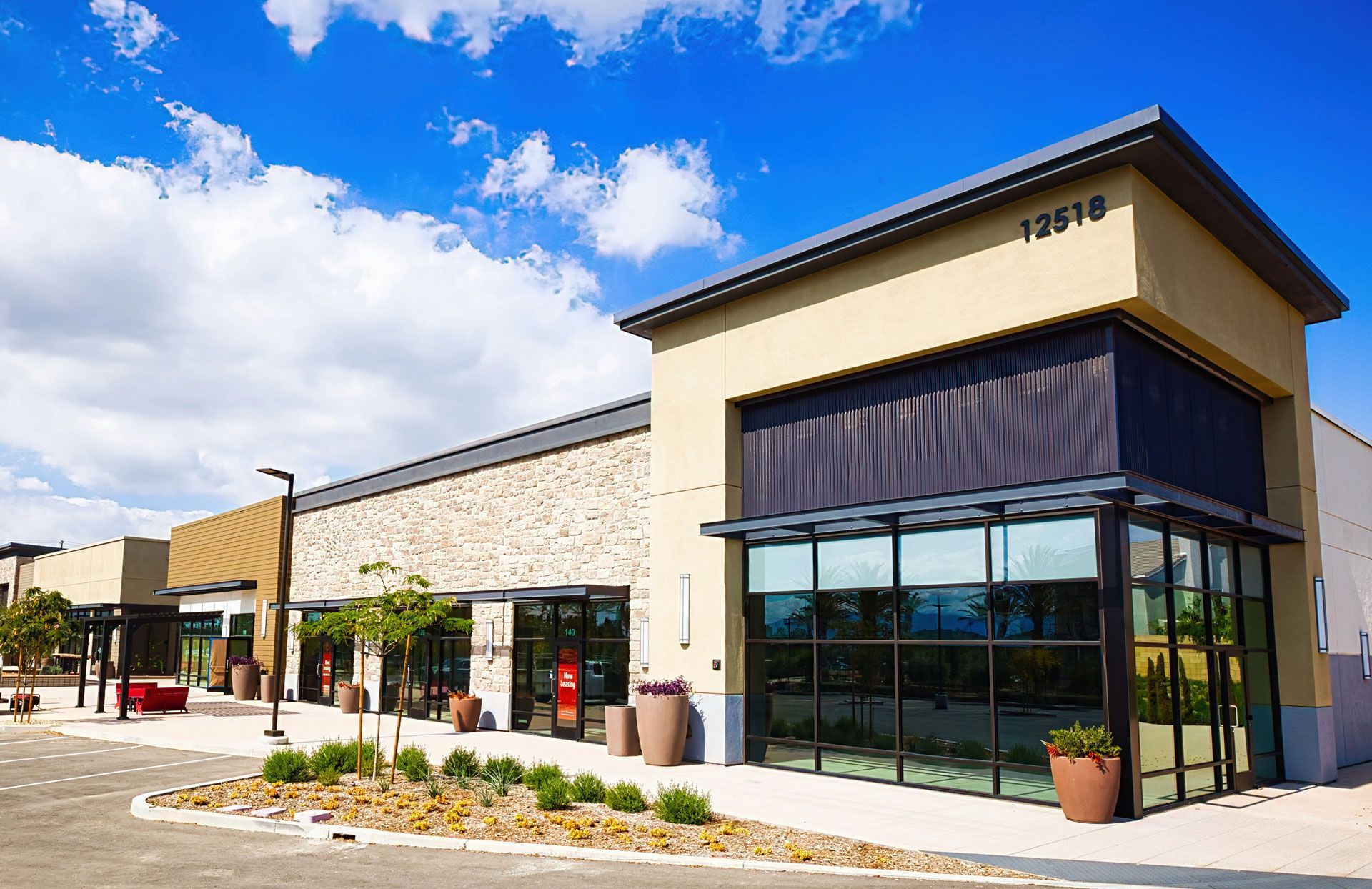 Exterior view of a commercial building with multiple storefronts under a blue sky. Beige and tan color scheme.