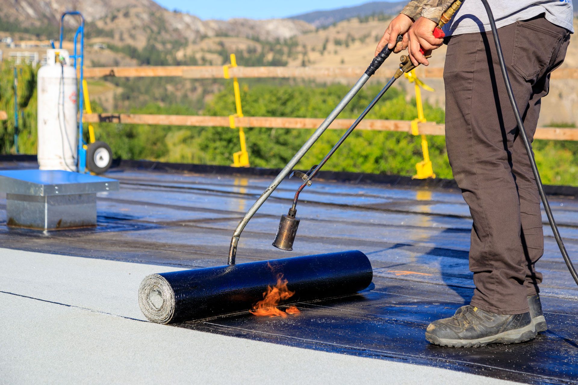 Person using a torch to install roofing material on a flat roof.