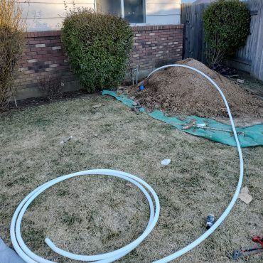 A large white pipe is sitting in the grass in front of a house.