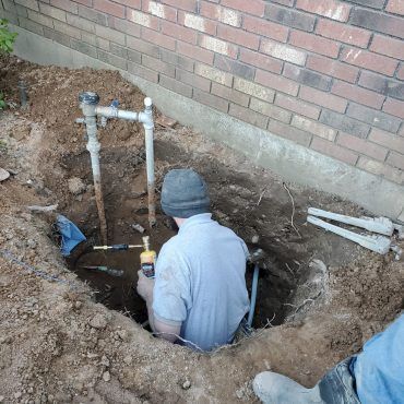 A man is sitting in a hole working on a pipe.
