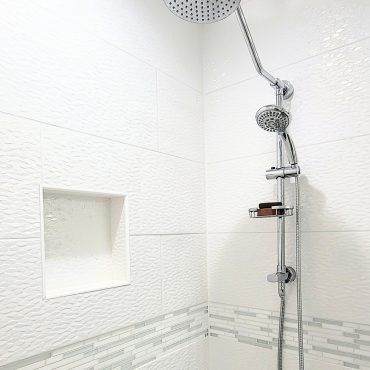A shower head in a bathroom with white tiles and a shelf.