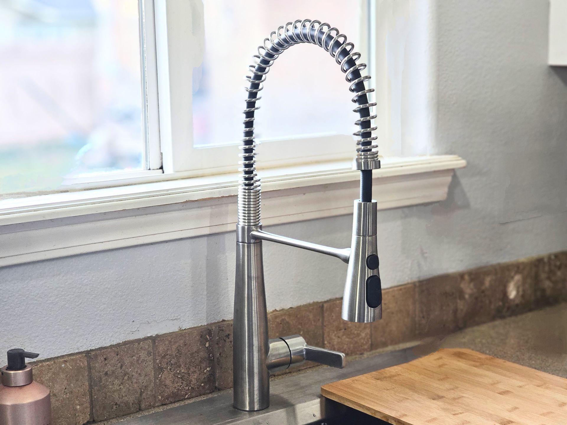A kitchen sink with a stainless steel faucet and a wooden cutting board
