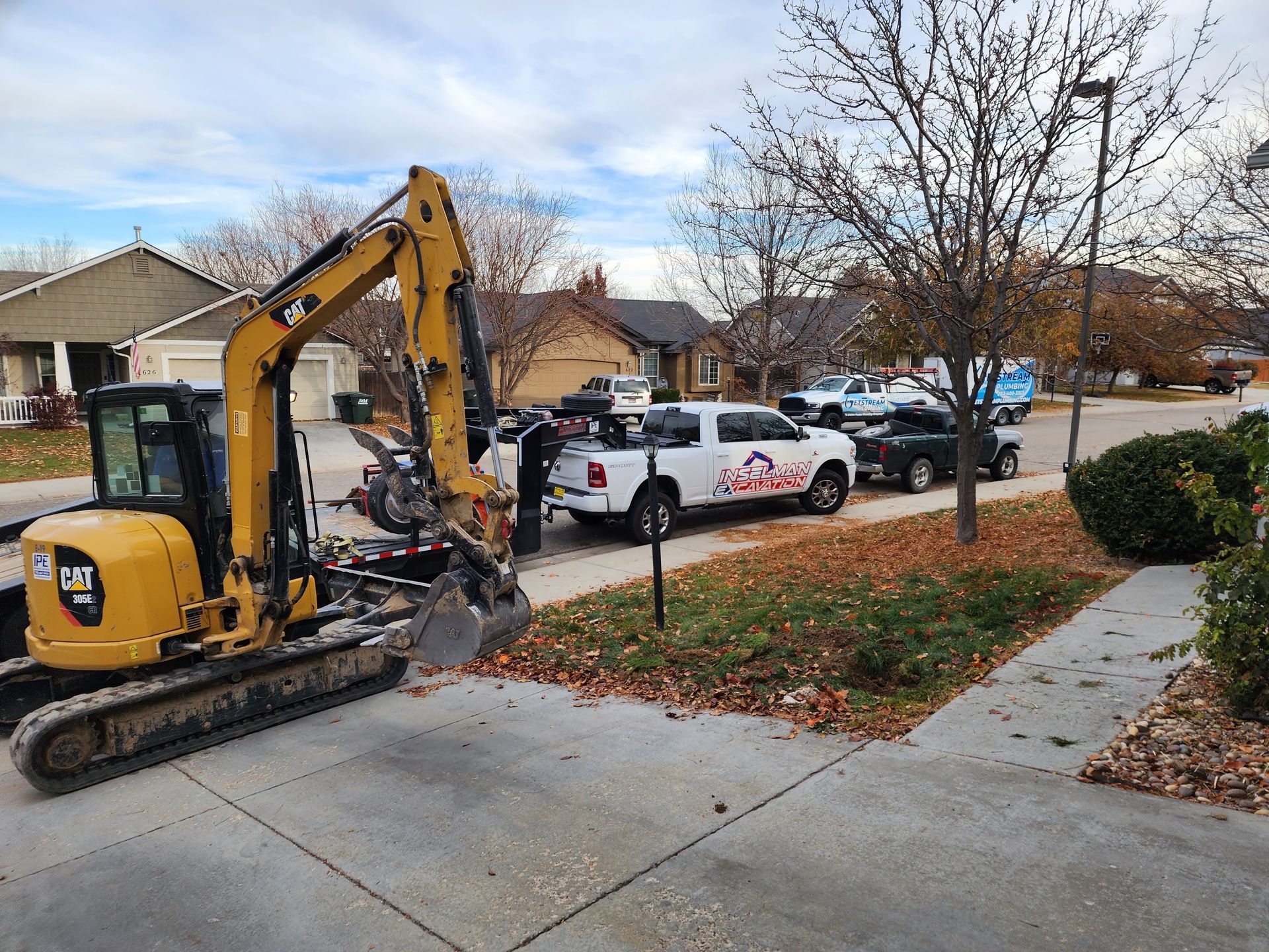 A yellow excavator is parked on the side of the road next to a white truck.