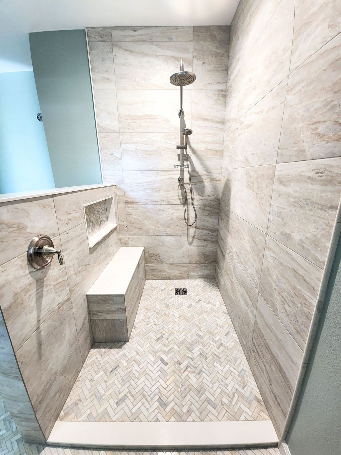 A shower with a bench and a shower head in a bathroom.