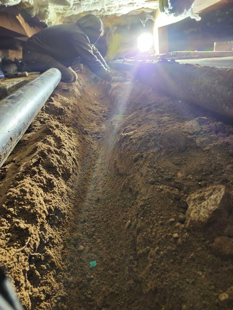A man is digging a hole in the ground under a house.