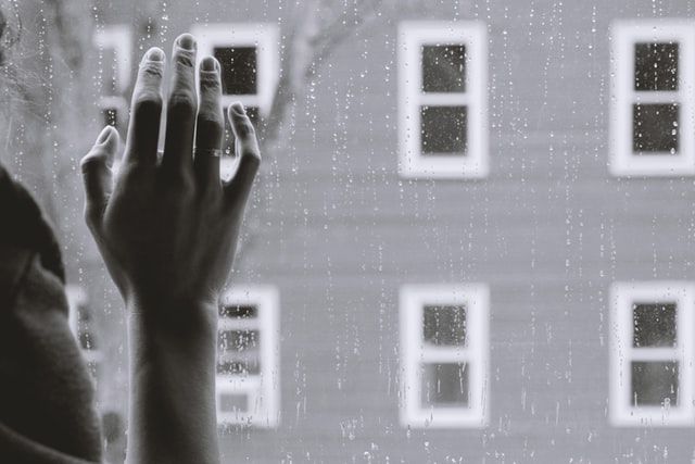 Person touching a rain-covered window in reflection and grief 