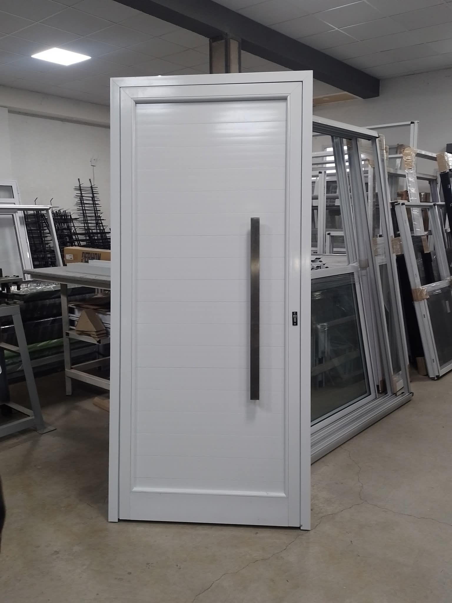 Puerta de entrada blanca con tirador largo negro. Interior con marcos metálicos al fondo.