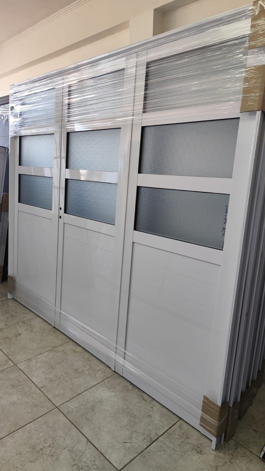 Puertas con marco blanco y paneles de vidrio esmerilado, apiladas en una habitación.