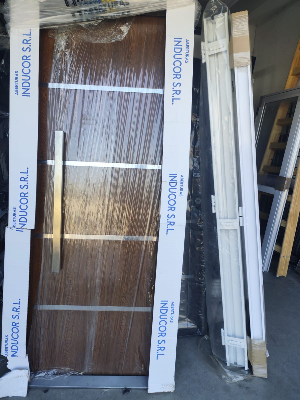 Puerta de madera con detalles en plata, envuelta en plástico, con moldura blanca.