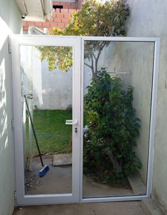 Puerta de vidrio con marco blanco, que conduce a un pequeño patio con césped y un árbol.