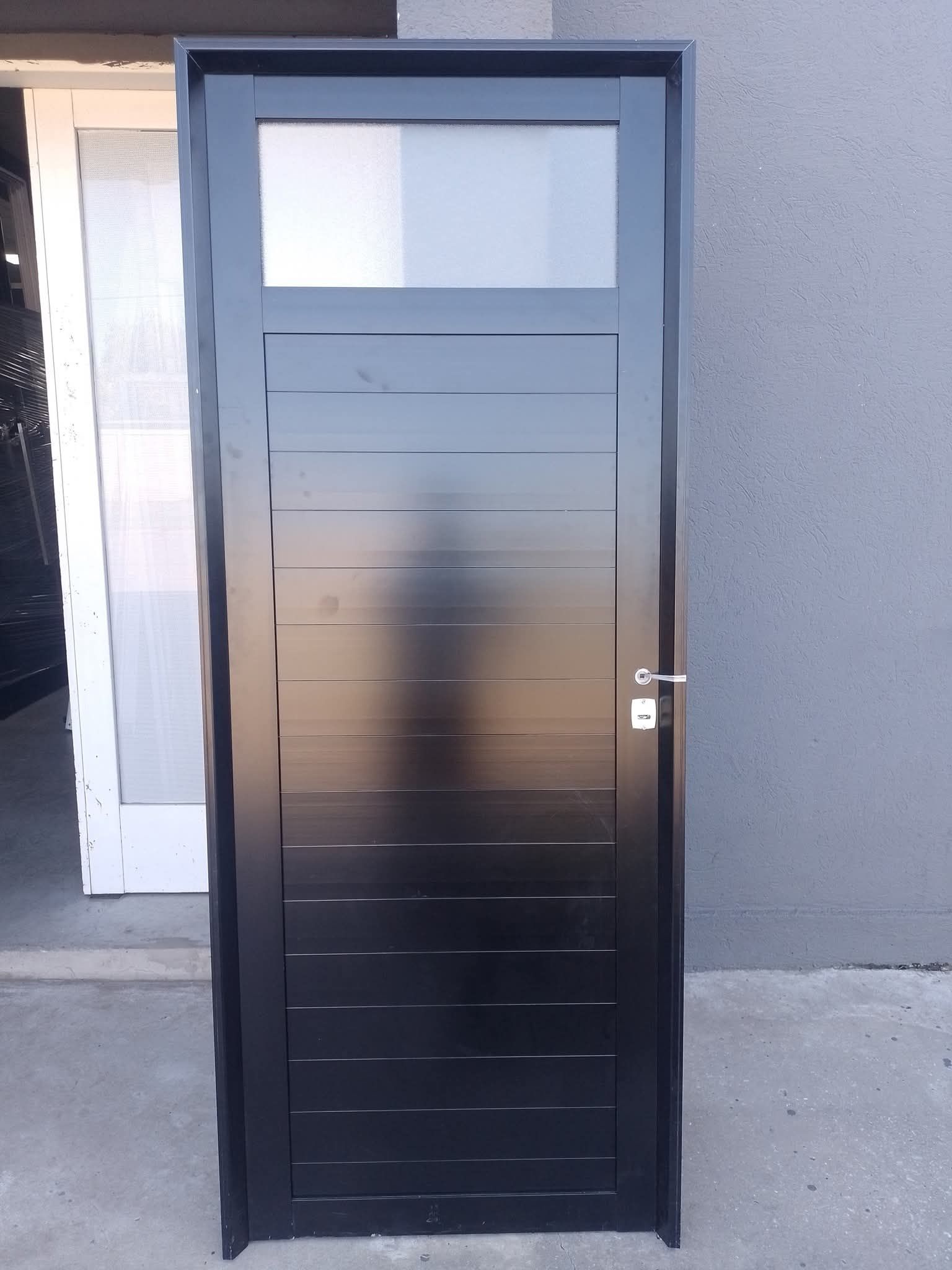 Puerta negra con un panel de vidrio esmerilado, situada contra una pared gris.