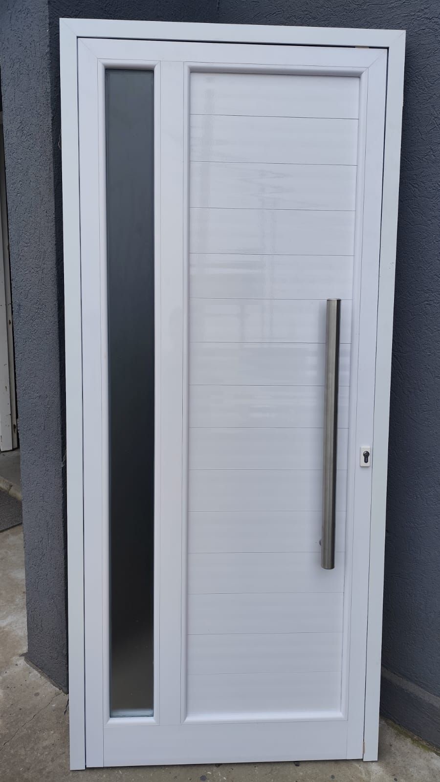 Puerta de entrada blanca con panel de vidrio esmerilado vertical y manija plateada larga.