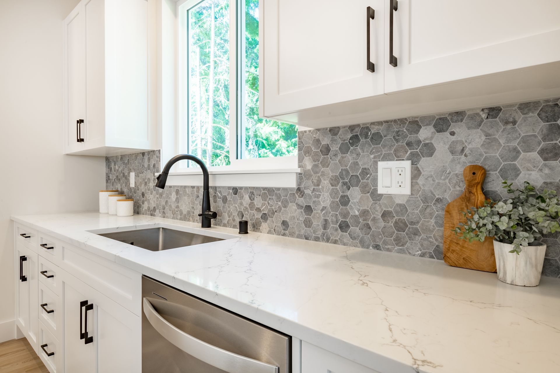 A kitchen with white cabinets , a sink , a dishwasher , and a window.