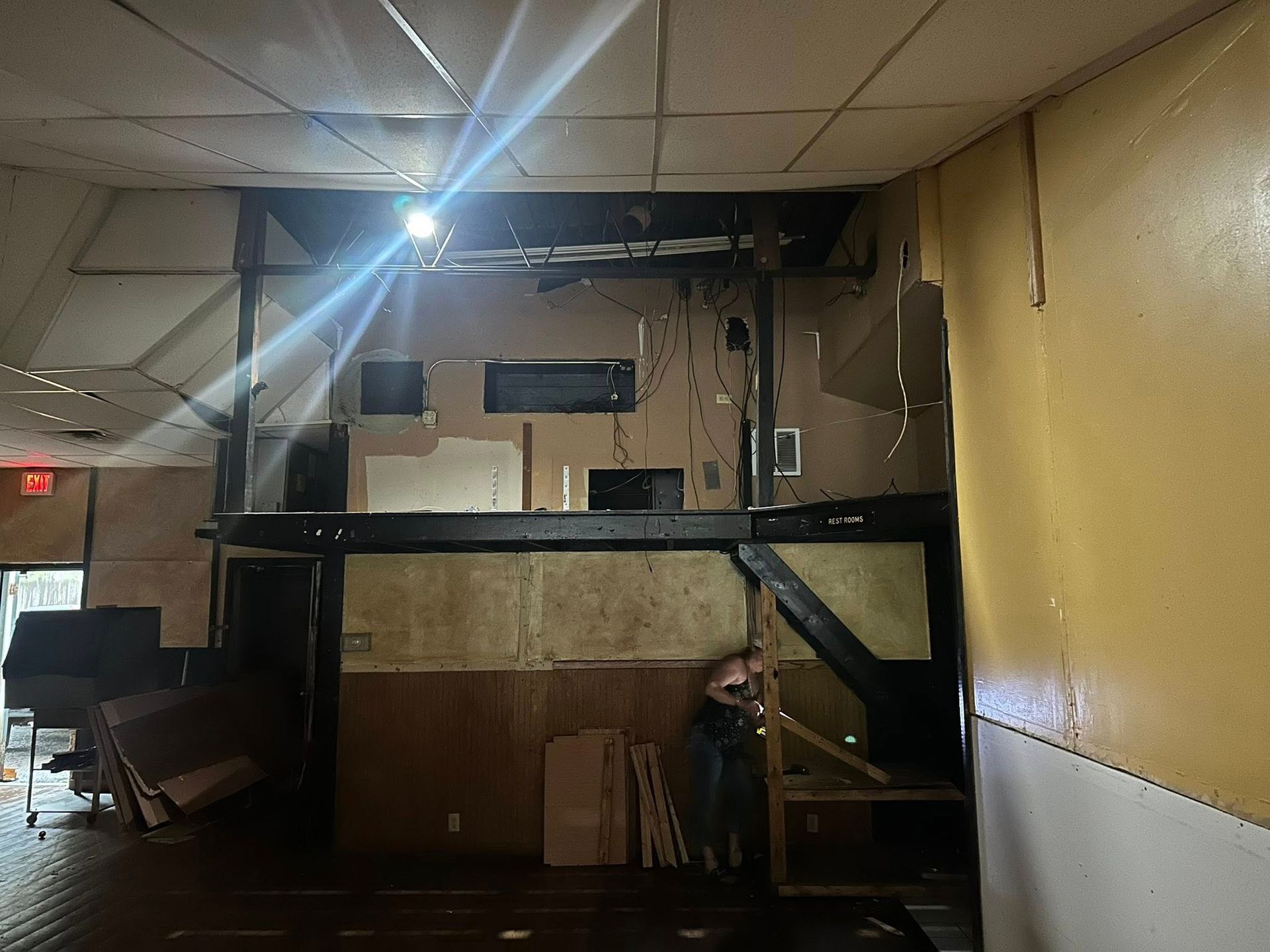 Interior view of a building with exposed beams and damage. A person stands near a staircase.